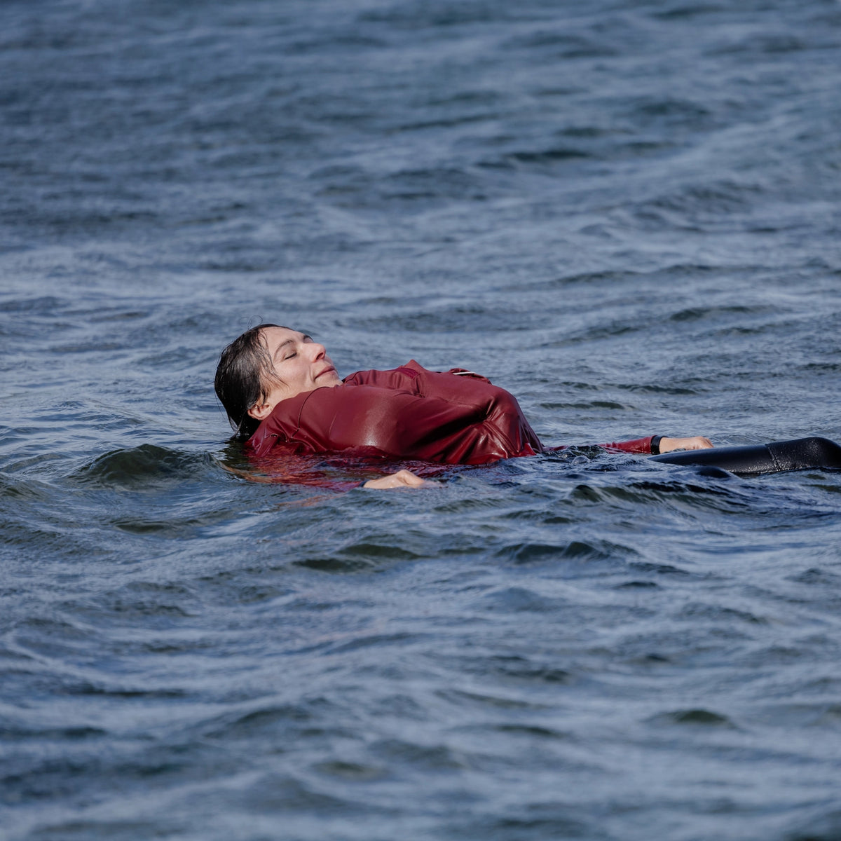 Woman at sea, in the water, wearing a Floatee anti-drowning T-shirt red with long sleeves with life jacket part being triggered
