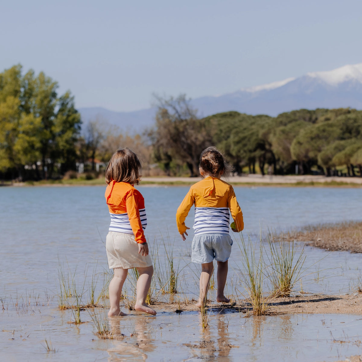Two children wearing Floatee anti-drowning T-shirts near a lake, rear view